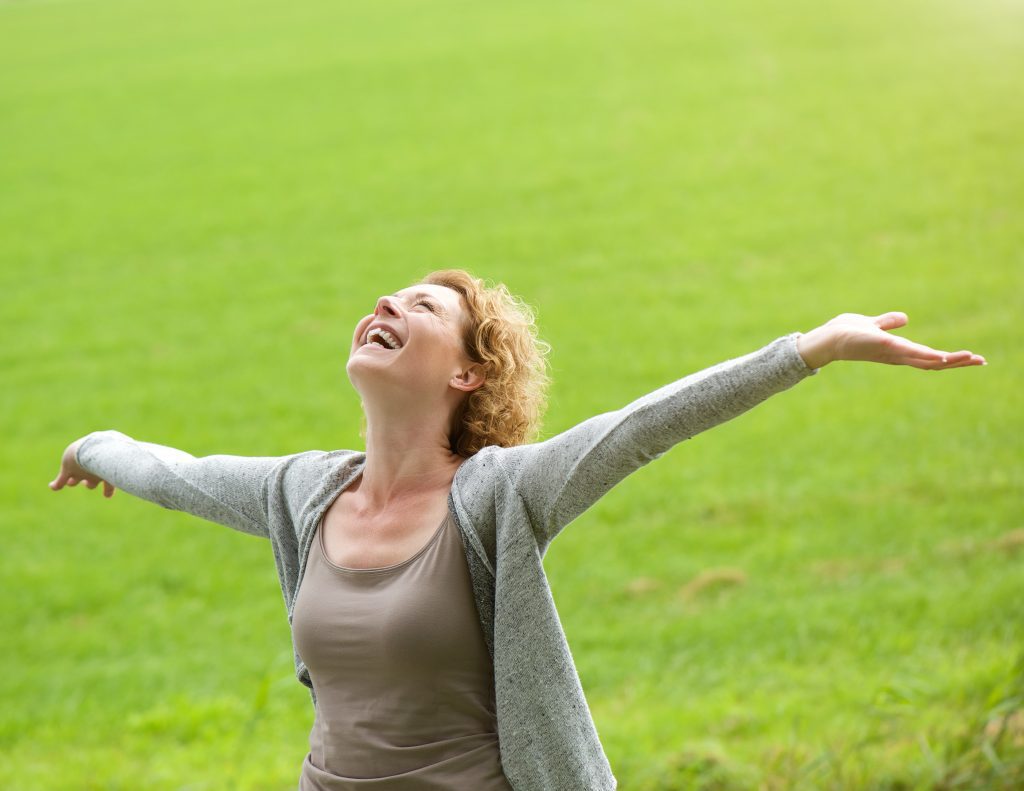 Woman finding God;s Joy surrounded by greem grass
