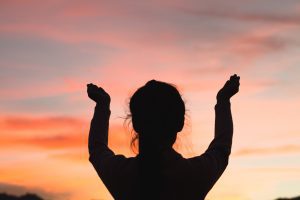 woman praising God at sunset. One of the Benefits of Faith is the Presence of God