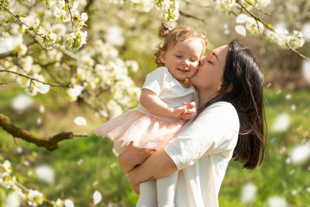 Mother and Child dressed in white with blooming tree of white flowers in background.