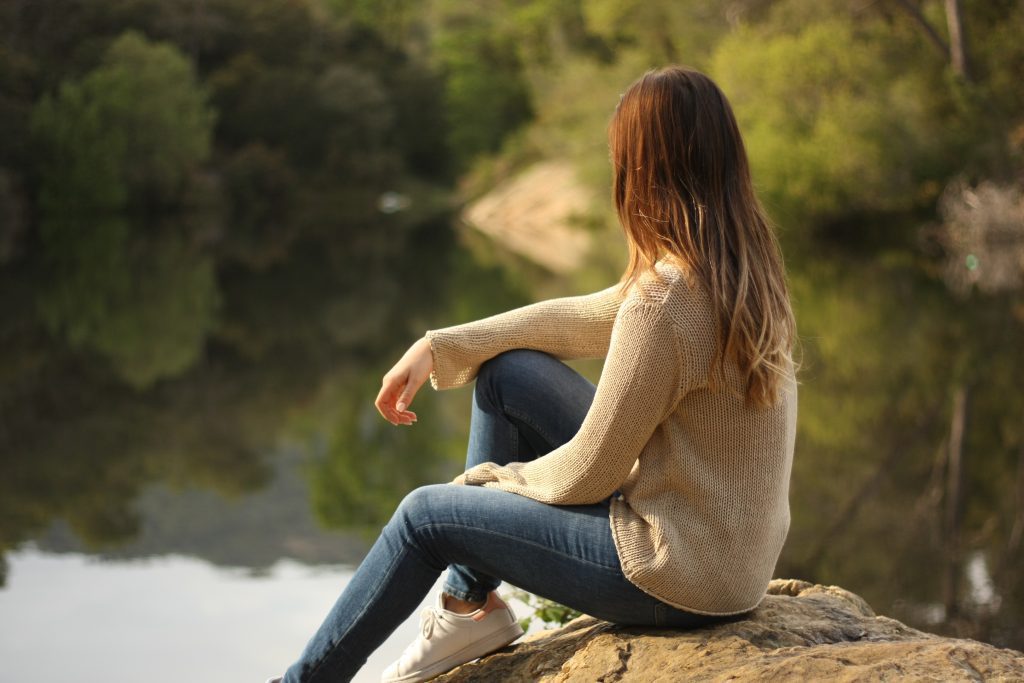 A woman by a lake peacefully looking out over the water. Finding God's peace in uncertain times